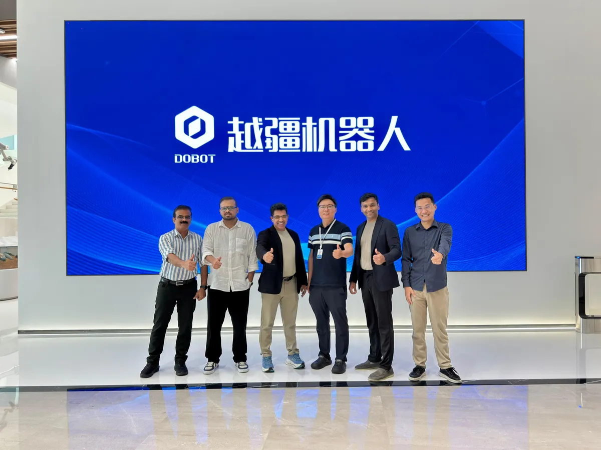 The Zeta42 and DOBOT teams stand together giving a thumbs-up in front of a large DOBOT screen.