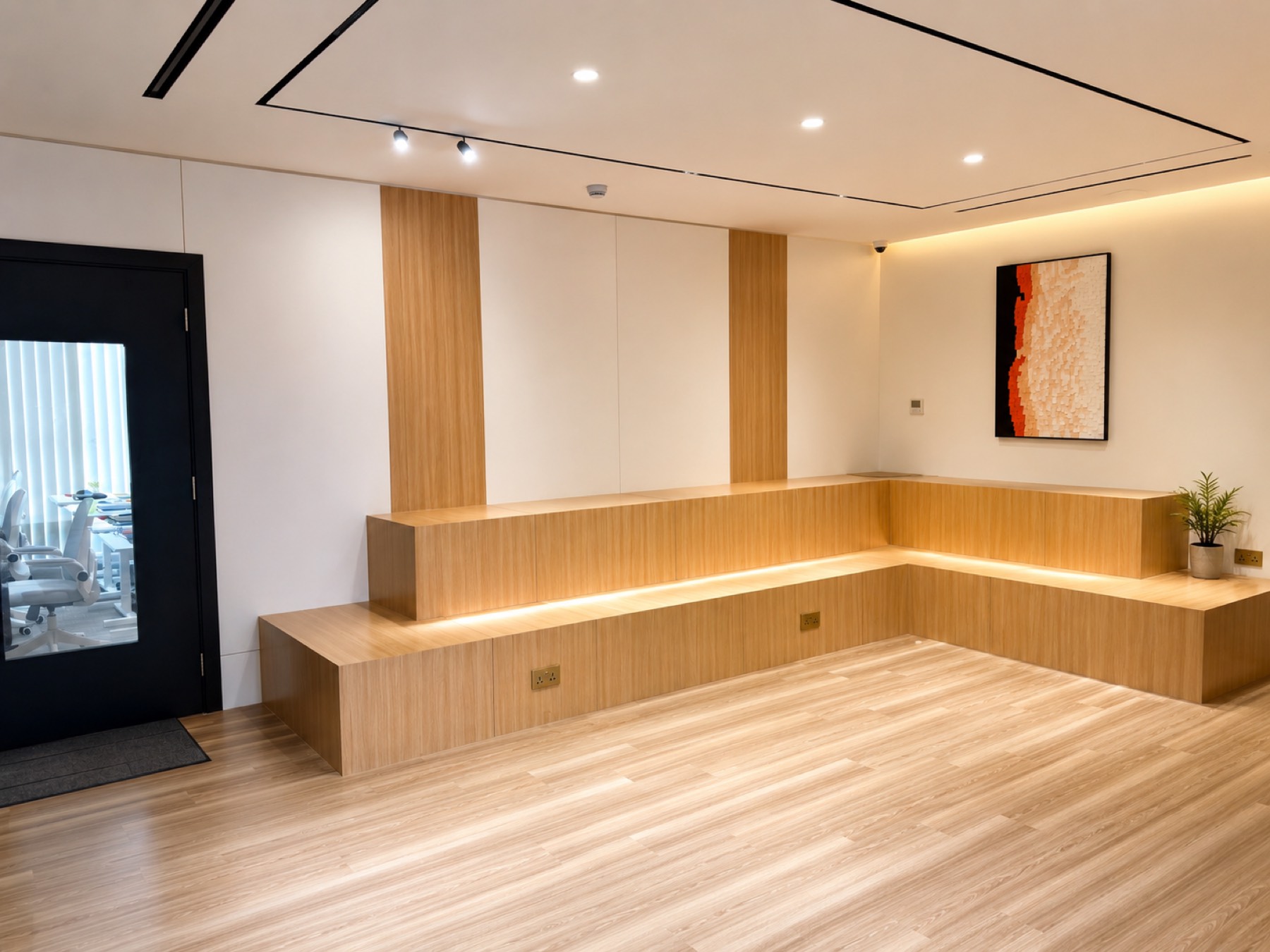 The campus lobby, a long run of pale wood bench seating under lit coving with a framed print on the end wall